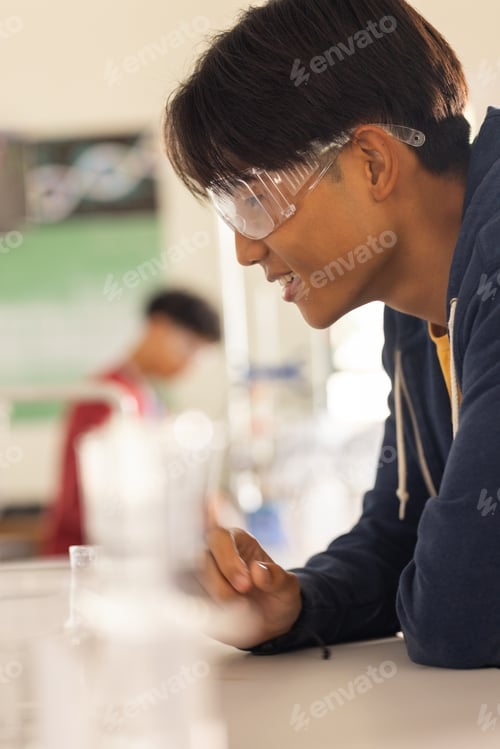 Preview: In high school, teenager wearing safety goggles conducting experiment in science class