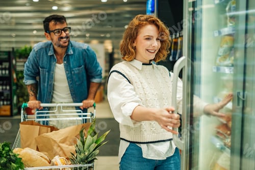 Preview: Couple shopping for groceries, choosing frozen food in supermarket refrigerator