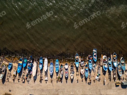 Preview: Numerous fishing boats lined up along the shoreline at sunrise, showcasing various colors and sizes