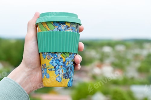 Preview: Male hand holding colorful mug with nature background. Drinking coffee from personal perspective.
