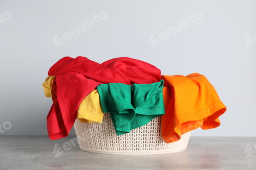 Preview: Laundry basket with clothes on grey table against light background. Space for text