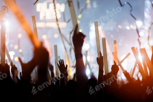 Preview: silhouettes of hand in concert.Light from the stage.confetti.the crowd of people silhouettes with th