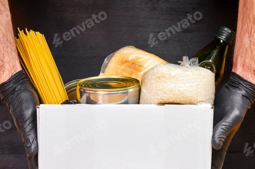 Preview: Close up mans hands in black rubber gloves holding a white box with pasta, cereals and canned food