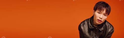 Preview: Stylish young man poses confidently against a vibrant orange background
