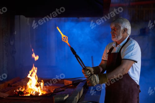 Preview: Mature industrial worker holding forceps with heated steel