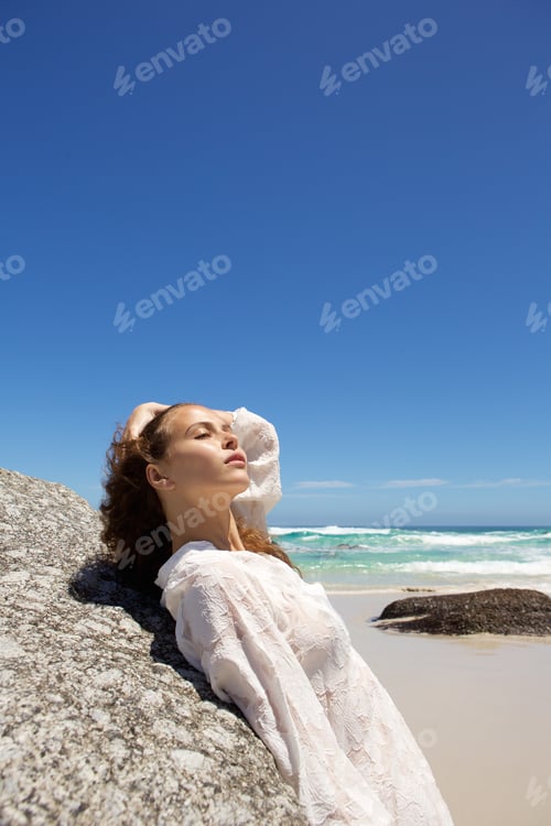 Preview: Attractive young woman leaning on rock at the beach