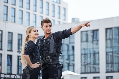 Preview: sporty strong man showing a modern building to a good looking girlfriend