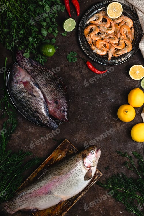 Preview: top view of raw fish, chili peppers, shrimp, herbs with lemons and tablecloth on dark table top