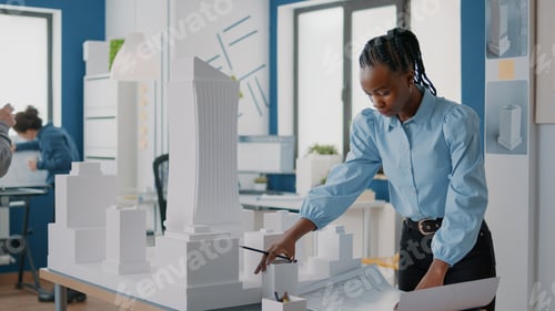Preview: African american architect analyzing blueprints plan and building model at work