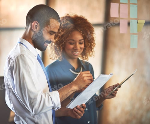 Preview: Shot of two young professionals brainstorming with sticky notes on a glass wall in an office