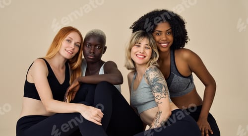 Preview: Four happy multicultural fit sporty girls sitting at beige background. Portrait