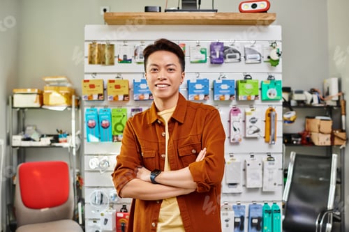 Preview: happy asian store manager smiling at camera near counter of private electronics shop, small business