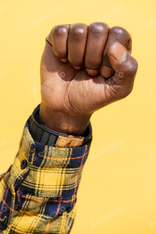 Preview: raised fist of african man on a yellow background