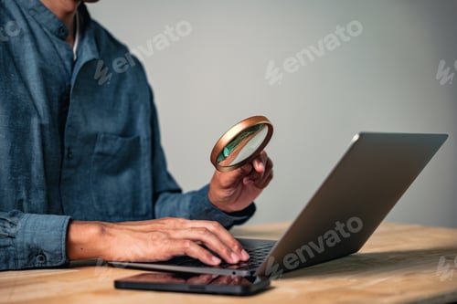 Preview: A man shows a hand gesture in a focused pose using a magnifier to inspect a laptop, a sign of