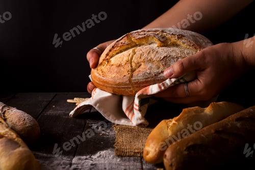Preview: Baker woman holding rustic organic loaf of bread in hands - rural bakery.