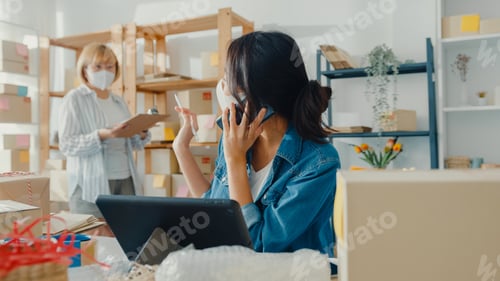 Preview: Asia businesswomen wear face mask using mobile phone call receiving purchase order and check.
