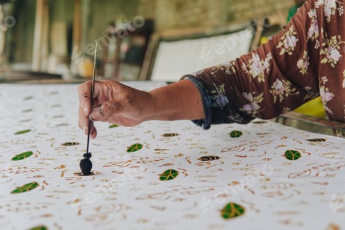 Preview: Close up picture of a person's hand drawing the design pattern of Indonesian batik tulis fabric.