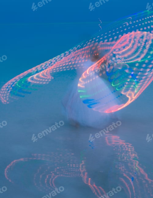 Preview: Swirling woman dancing with illuminated multi-coloured hoop at dusk