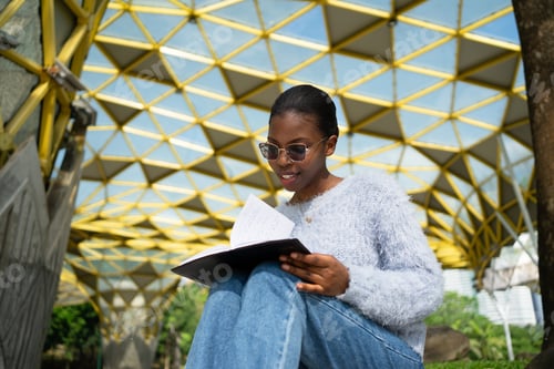 Preview: Young woman reading a book sitting in a modern park