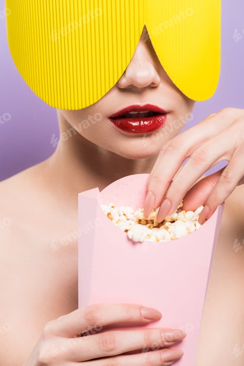 Preview: young woman holding bucket with salty popcorn isolated on purple