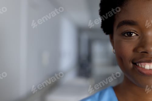 Preview: Portrait of happy african american female doctor wearing scrubs in corridor at hospital, copy space