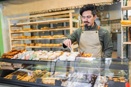 Preview: Baker arranging pastries in display case at bakery shop