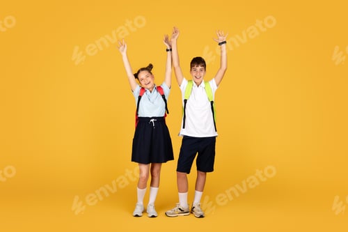Preview: Glad caucasian teen girl and boy pupil raising hands up, celebrating victory and success