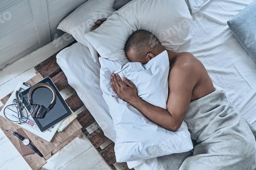 Preview: What is he dreaming about? Top view of young African man sleeping while lying in the bed at home