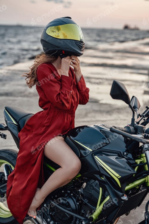Preview: Slim woman biker wearing helmet on bike against seascape