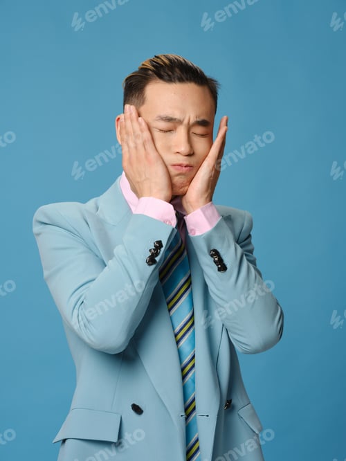 Preview: man in a classic suit touching his face with his hands on a blue background