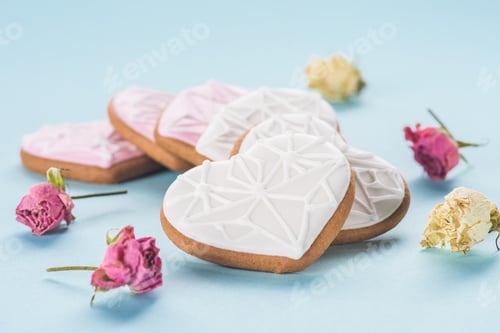 Preview: close up view of heart shaped cookies and decorative flowers isolated on blue