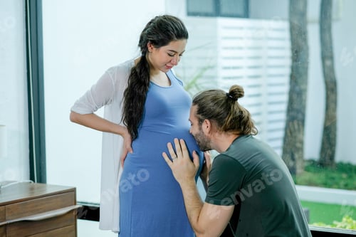 Preview: Pregnant woman stand and look to her husband who kiss belly and stay together