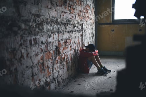 Preview: Sad and disappointed teenagers boy sitting indoors in abandoned building.