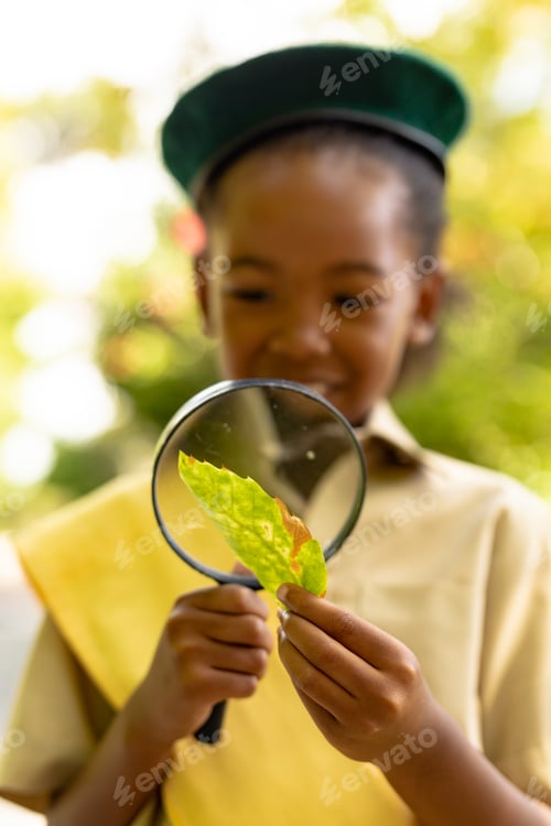 Preview: African american scout girl looking at leaf through magnifying glass in forest