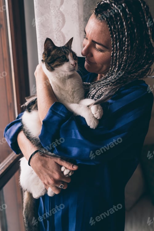 Preview: Adult woman indoors at home posing window hugging cat