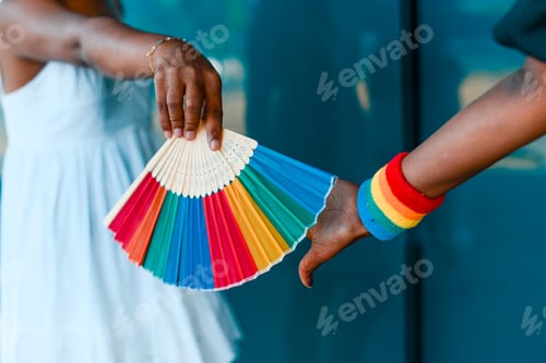 Preview: Human hands hold LGBTQ pride fan and wristband