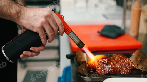 Preview: Chef hands using blowtorch searing meat in a dark professional kitchen workflow