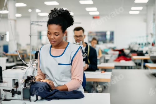 Preview: Young black seamstress working at sewing production line in a factory.