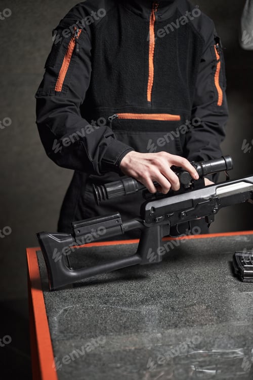 Preview: Young Adult Man Assembling Rifle Scope on Table Indoors