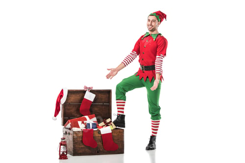 Preview: smiling man in christmas elf costume standing near wooden chest full of presents with outstretched