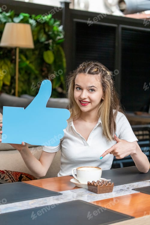 Preview: Adorable girl holding idea board and pointing finger to her coffee