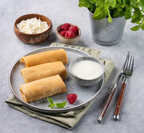 Preview: Homemade crepes with raspberry and sour cream on a plate on a light background with mint.