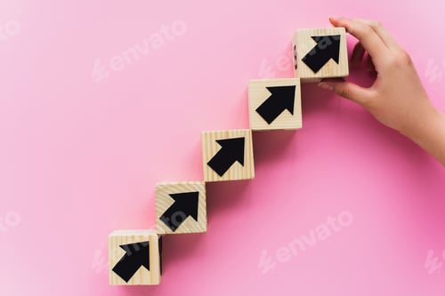 Preview: partial view of hand near wooden blocks with black arrows on pink background, business concept