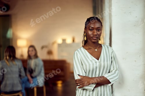Preview: Confident Woman Standing Indoors with People Conversing in Background