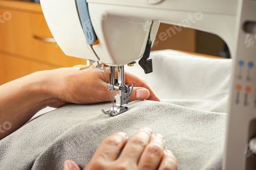 Preview: Female hands stitching gray fabric on modern sewing machine. Close up view of sewing process.