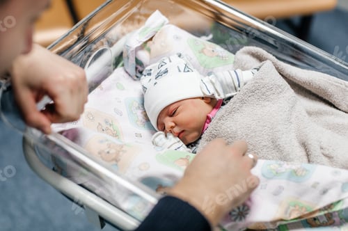 Preview: A newborn baby is lying in a crib, his father's hands are stroking him