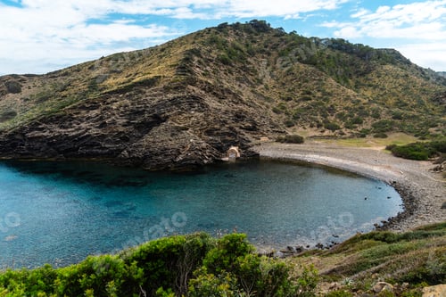 Preview: Scenic view of a secluded cove in Menorca with crystal clear waters and lush greenery.
