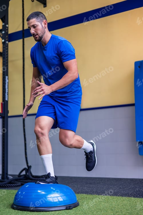 Preview: vertical young athlete performing leg and balance workout with Bosu ball at gym