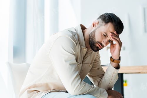 Preview: handsome upset man sitting and touching head in office