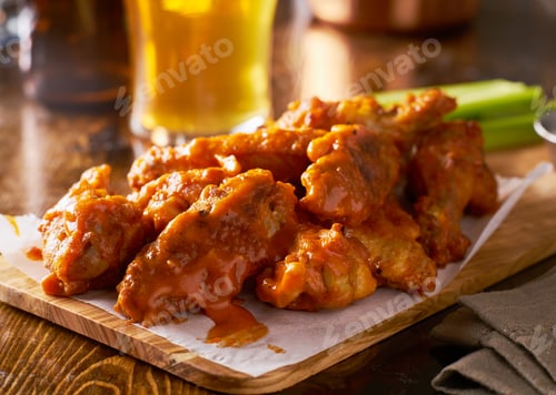 Preview: sauced buffalo chicken wings on wooden board with celery